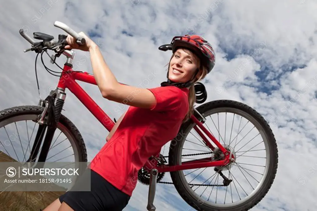 Germany, Bavaria, Young woman carrying mountain bike