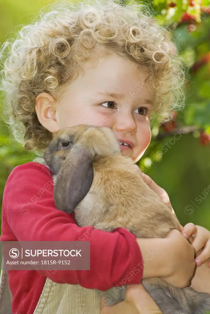 Blonde girl (4-5) with curly hair holding rabbit, portrait