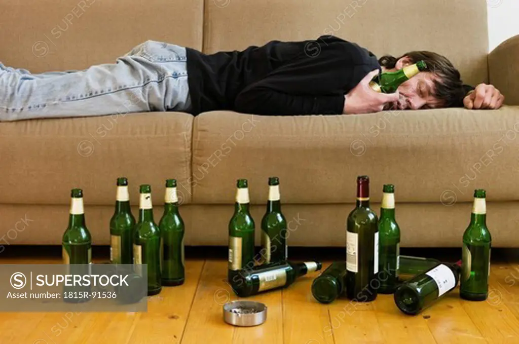 Germany, Hessen, Frankfurt, Drunk man lying on sofa with empty beer bottles