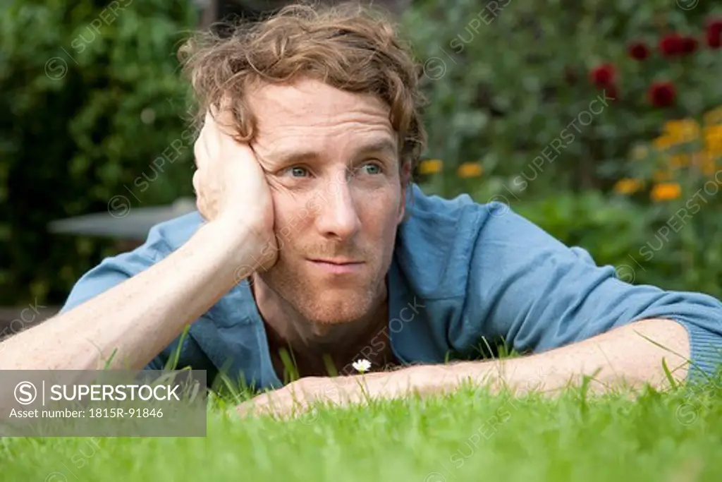 Man thinking while lying on grass in front of daisy