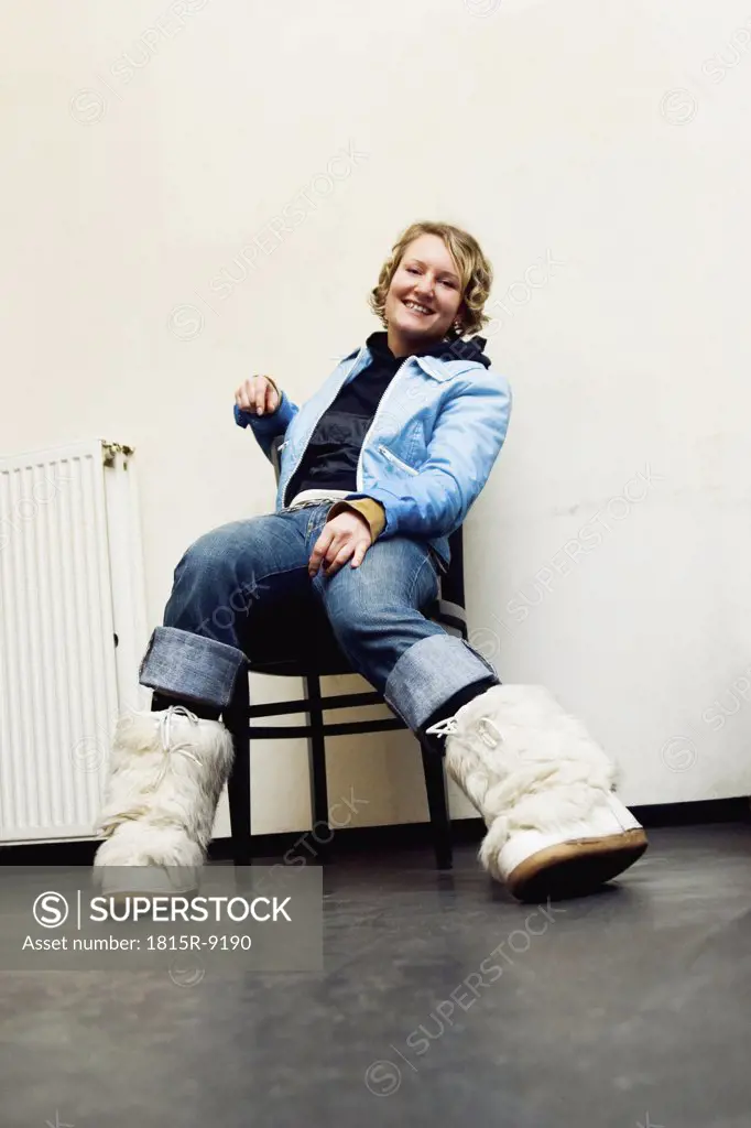 blond girl with short hair and a blue retro jacket sitting on a chair