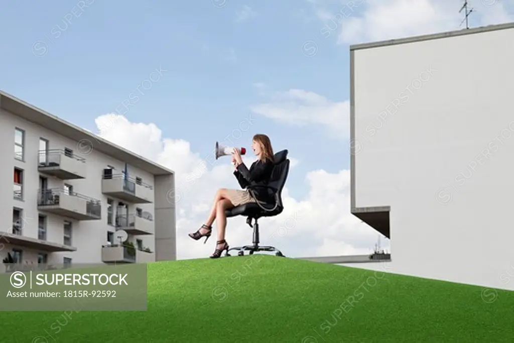 Germany, Bavaria, Munich, Businesswoman sitting on office chair and shouting through maghaphone