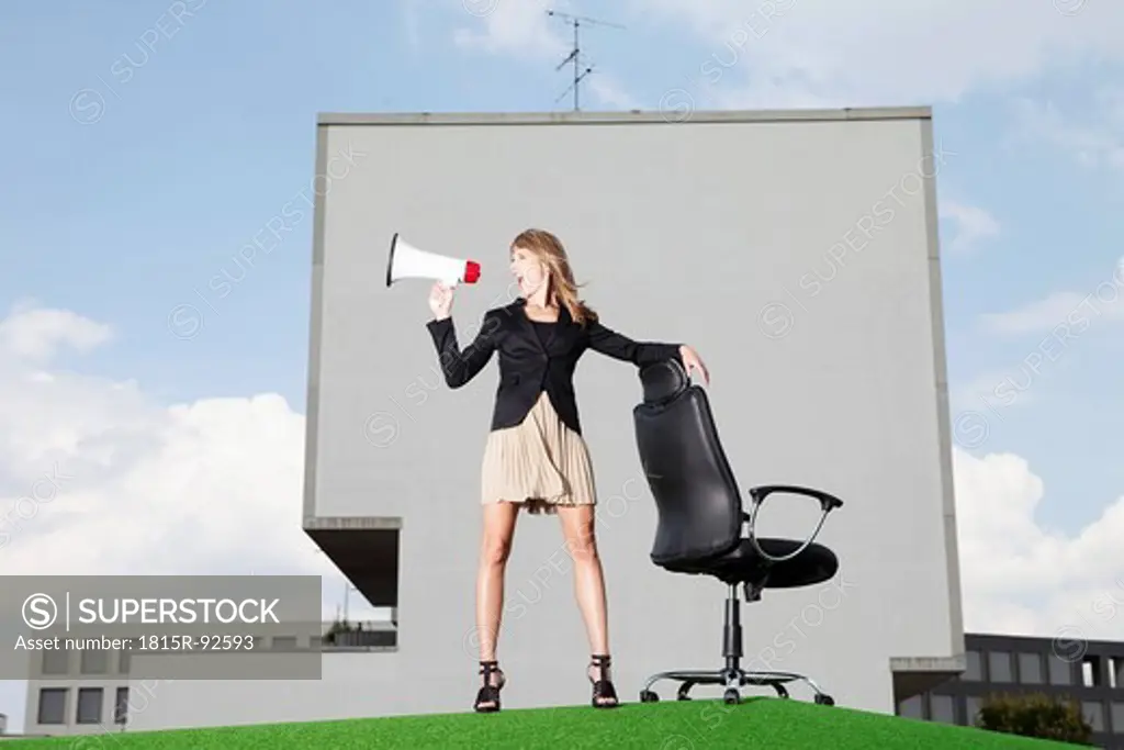 Germany, Bavaria, Munich, Businesswoman shouting through meghaphone in lawn
