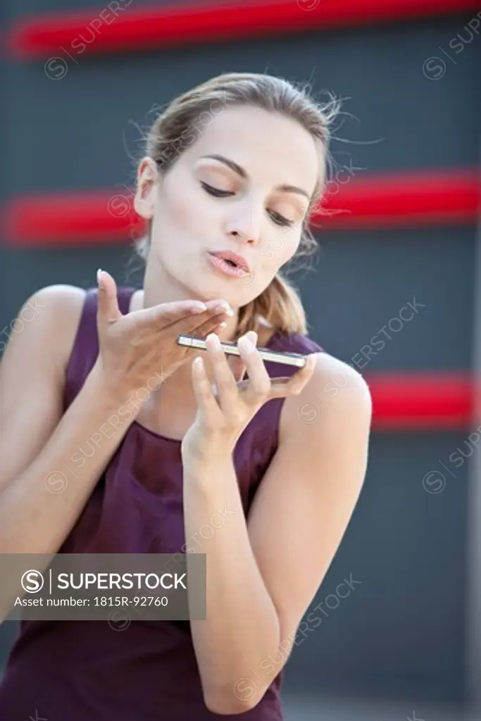 Germany, Bavaria, Young woman with cell phone blowing kiss