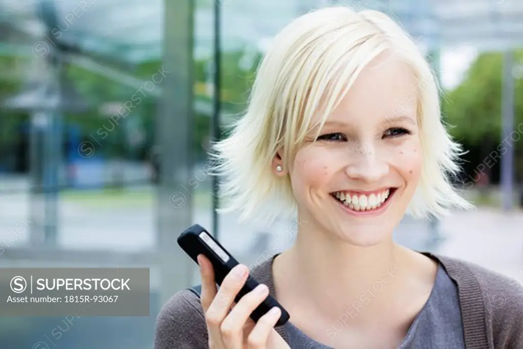 Germany, Bavaria, Munich, Young woman with cell phone, smiling