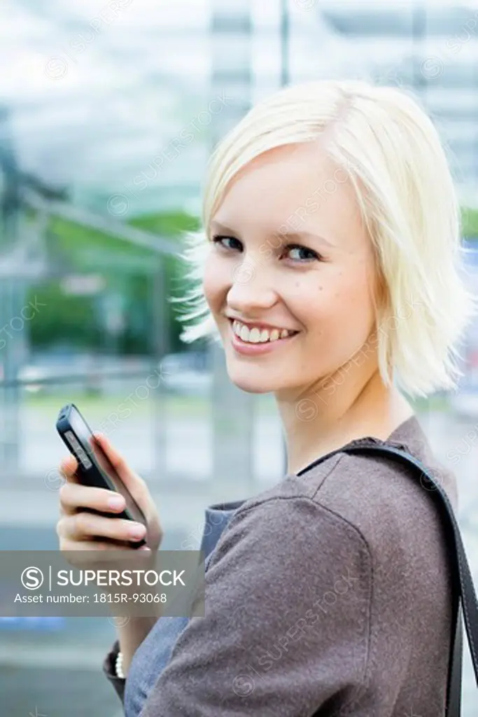 Germany, Bavaria, Munich, Young woman with cell phone, smiling, portrait