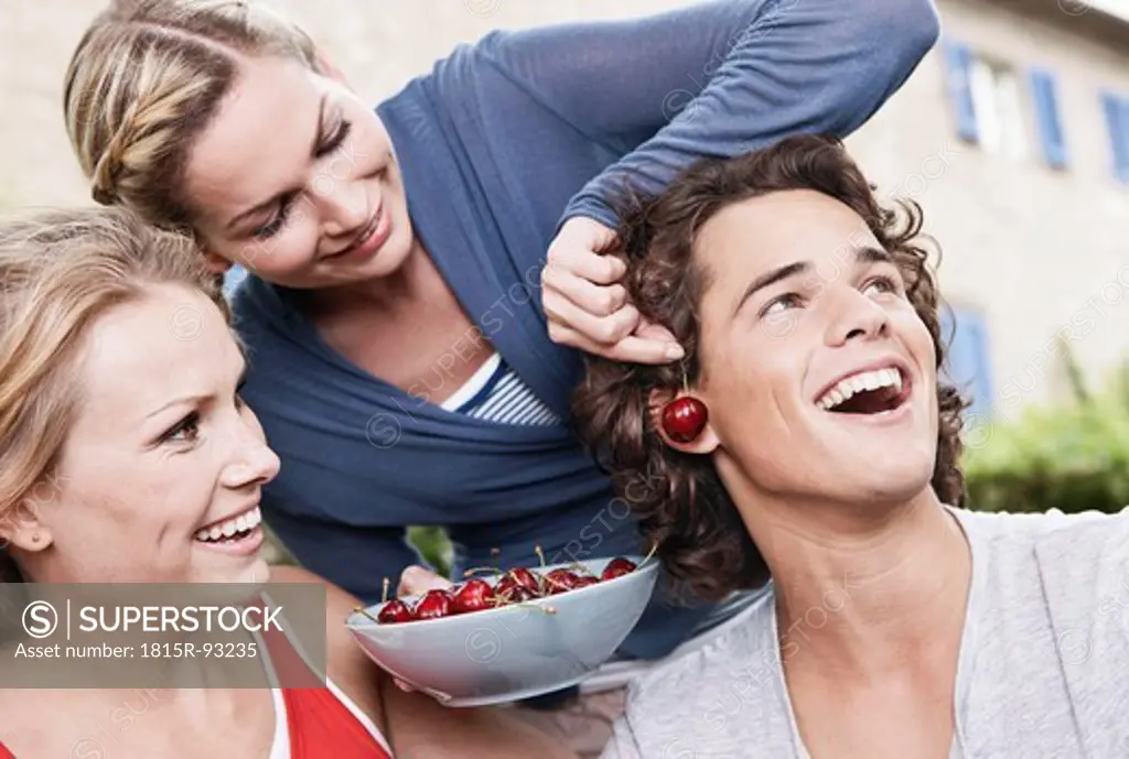 Italy, Tuscany, Magliano, Young man and women holding bowl of cherries and having fun, smiling