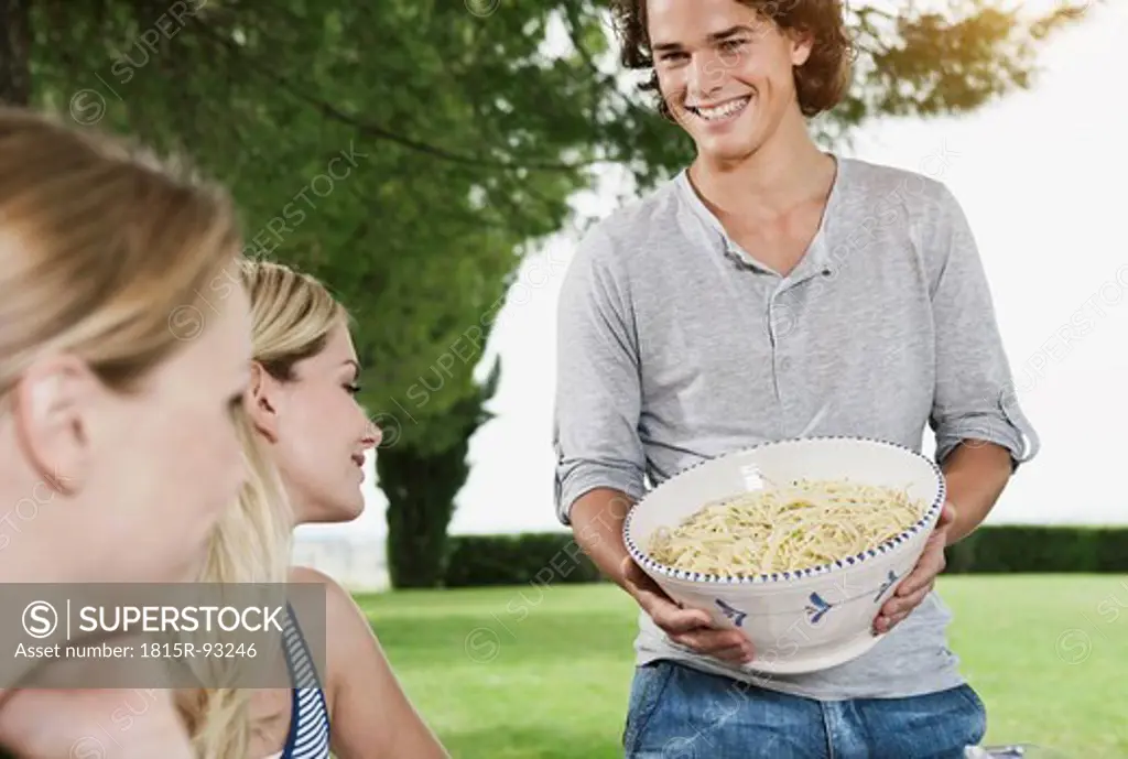 Italy, Tuscany, Magliano, Young man holding bowl of pasta and women in foreground, smiling