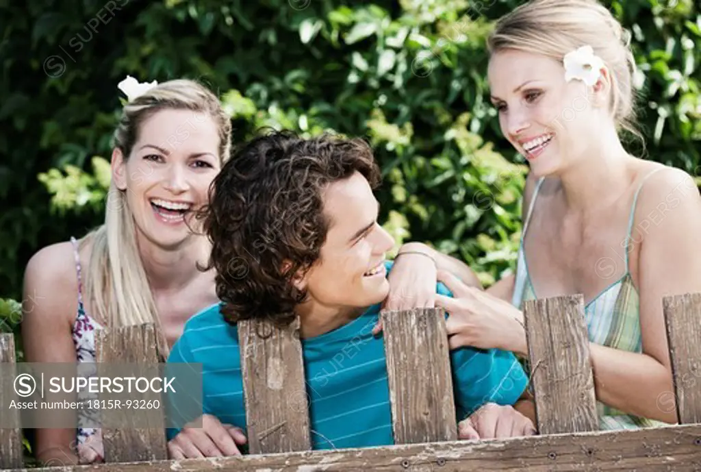 Italy, Tuscany, Magliano, Young man and women standing behind wood fence, smiling