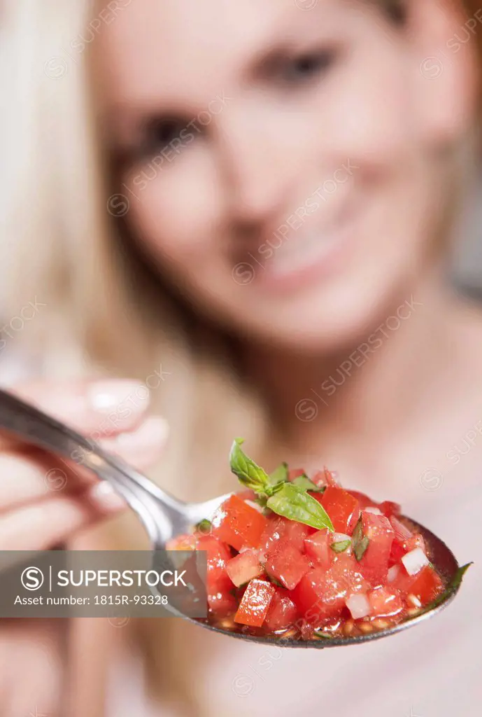 Italy, Tuscany, Magliano, Young woman holding spoon of chopped tomatoes