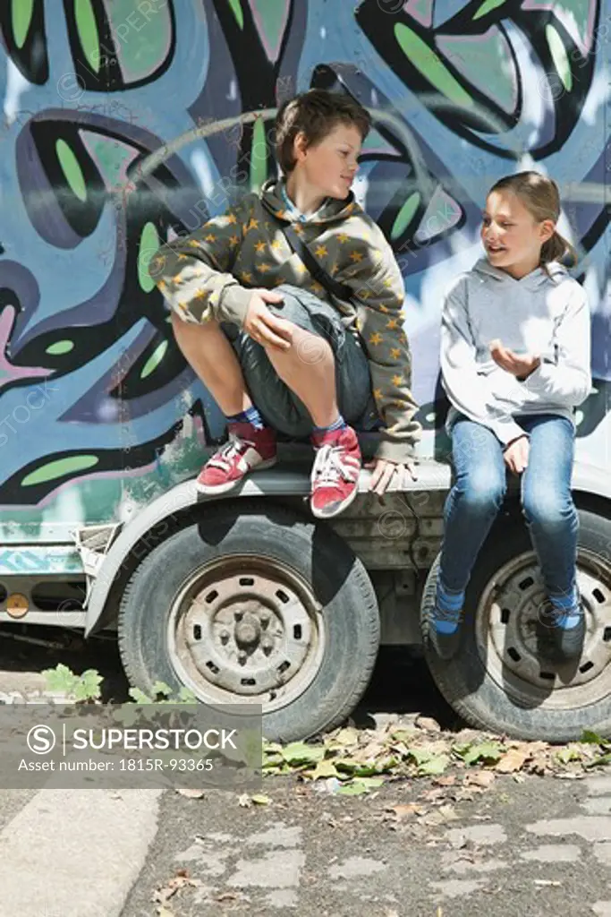 Germany, Berlin, Boy and girl sitting on graffiti truck
