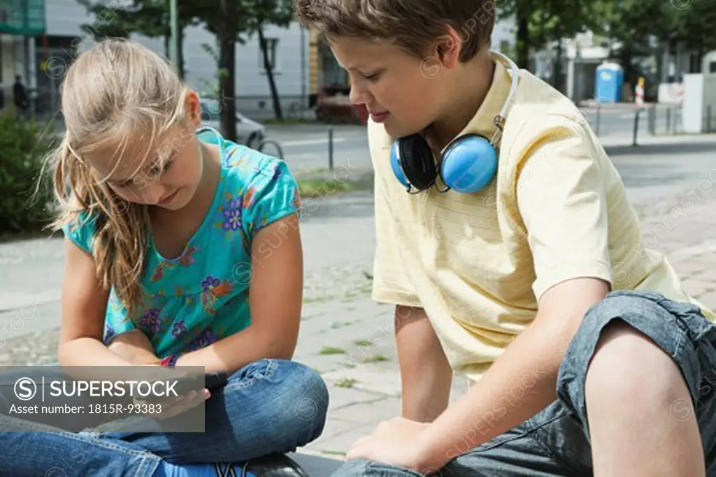 Germany, Berlin, Boy and girl sitting with cell phone and headphone
