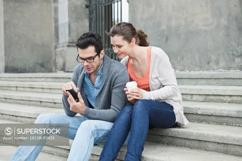 Germany, Berlin, Couple using cell phone on stairway