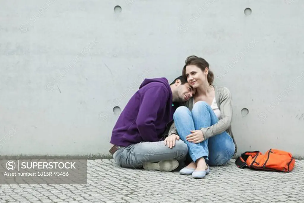 Germany, Berlin, Couple sitting in front of large wall on sidewalk