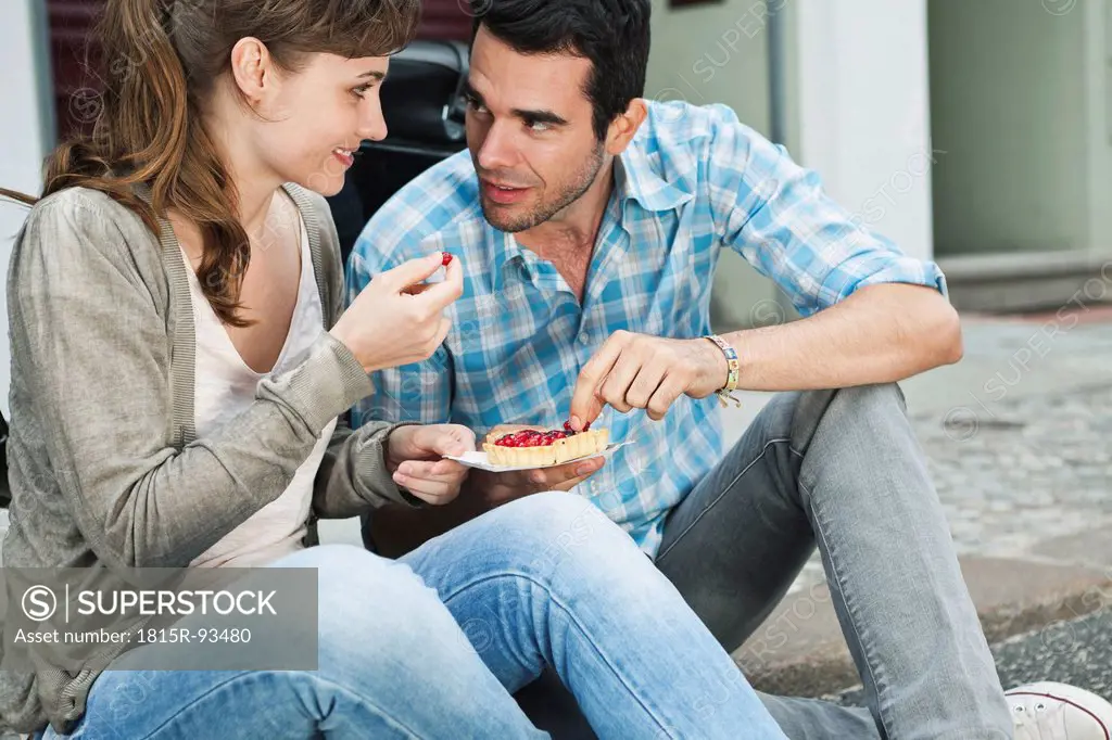 Germany, Berlin, Couple eating snacks on sidewalk