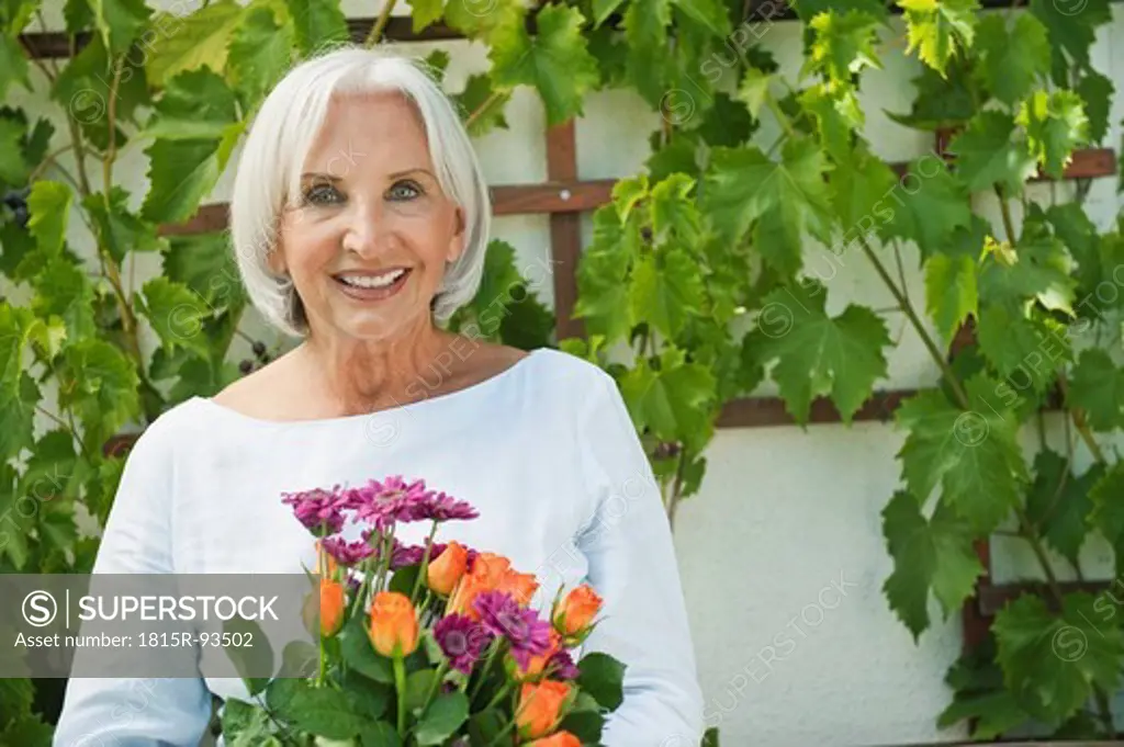 Germany, Bavaria, Senior woman holding flowers, smiling, portrait