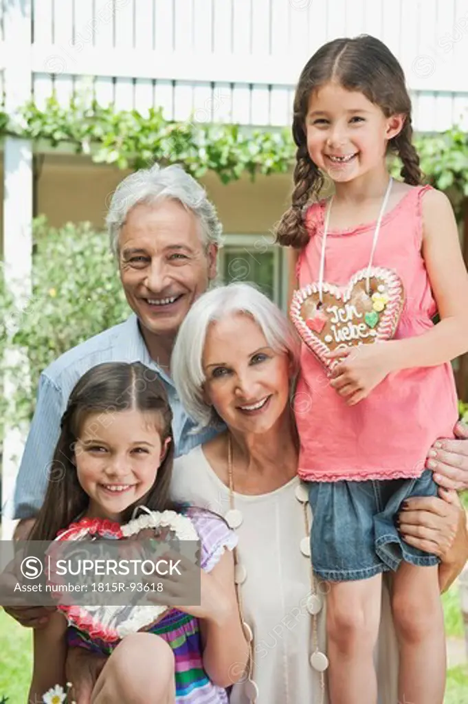 Germany, Bavaria, Grandparents with granddaughter holding gingerbread, smiling, portrait
