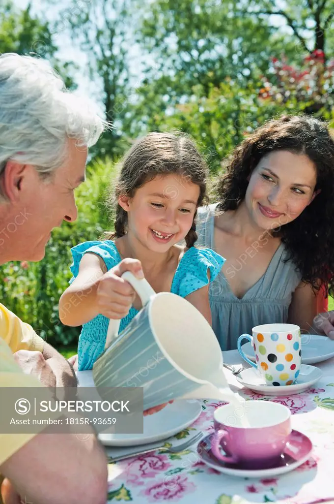Germany, Bavaria, Family having coffee and cake in garden, smiling