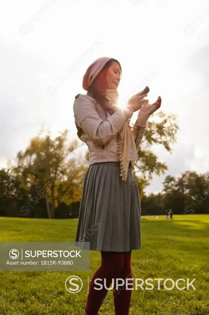 Germany, Cologne, Young woman with cell phone in park