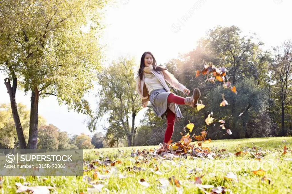 Germany, Cologne, Young woman playing in park with leaves, smiling