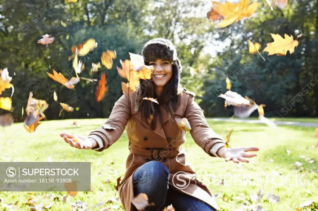 Germany, Cologne, Young woman playing in park with leaves, smiling, portrait