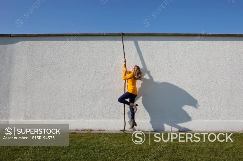 Germany, Bavaria, Munich, Young woman climbing wall with rope
