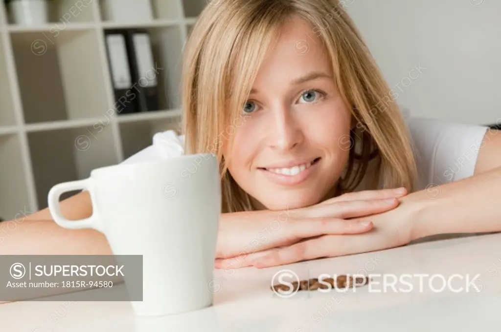 Young woman with coffee cup and beans, smiling, portrait
