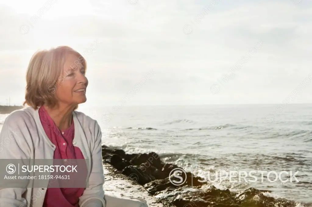 Spain, Mallorca, Senior woman sitting at sea shore, smiling