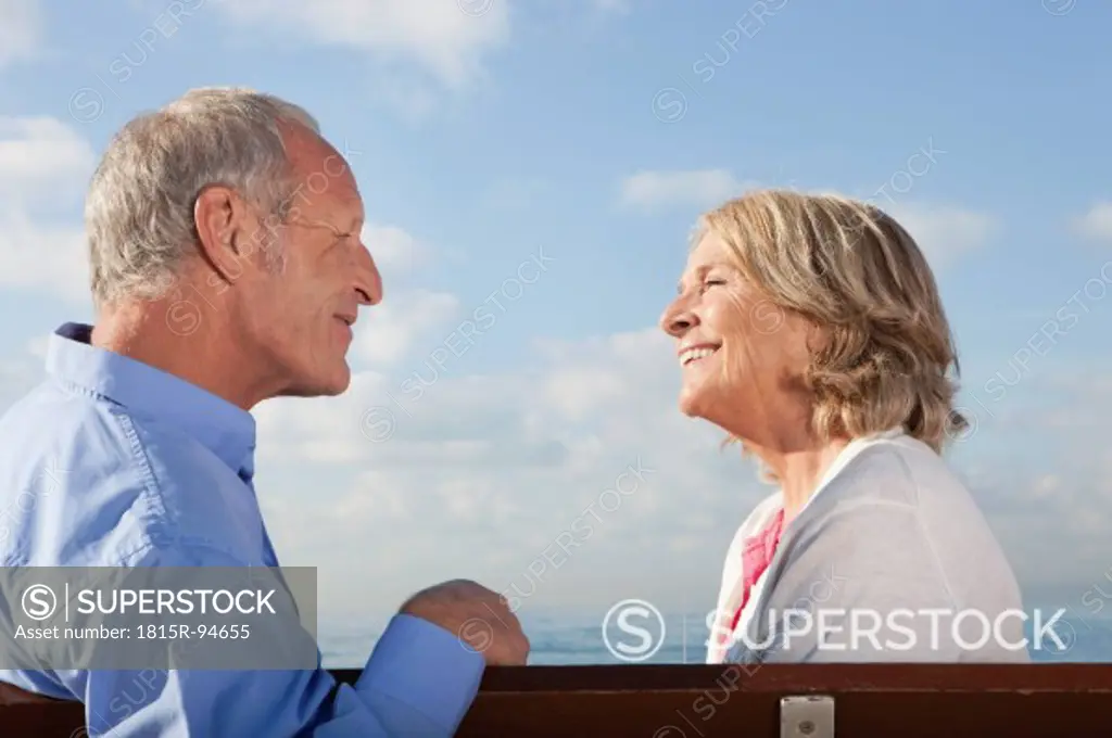 Spain, Mallorca, Senior couple sitting on bench at sea shore, smiling