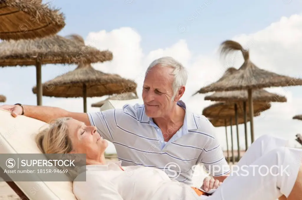 Spain, Mallorca, Senior man looking at woman resting on deck chair at beach