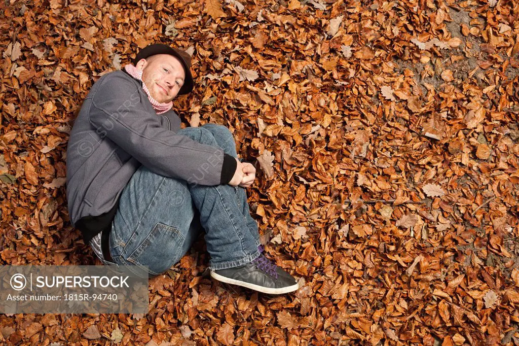 Germany, Berlin, Wandlitz, Young man lying in foliage, smiling, portrait