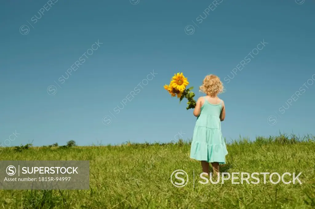 Germany, Bavaria, Girl standing in grass with sunflower