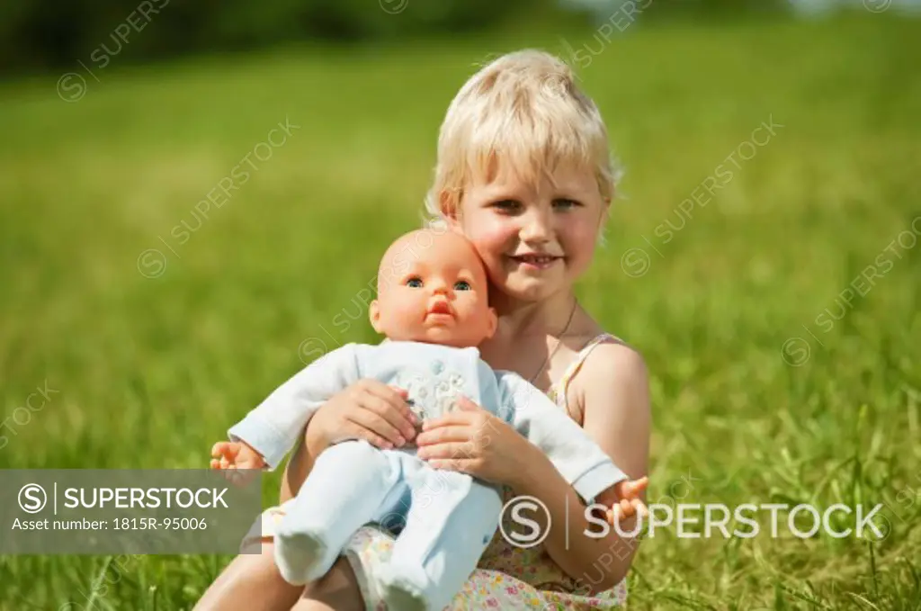 Germany, Bavaria, Girl with baby doll in grass, smiling, portrait