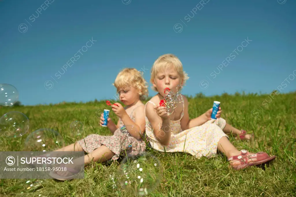 Germany, Bavaria, Girls sitting in grass and blowing bubbles