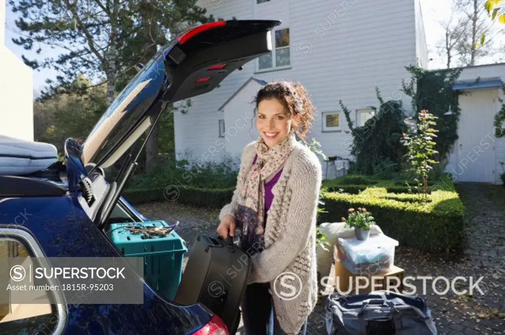 Germany, Bavaria, Grobenzell, Mid adult woman loading car trunk, smiling, portrait