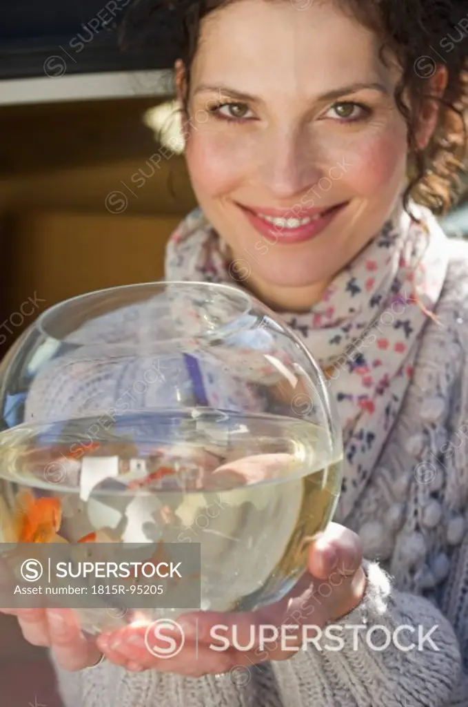 Germany, Bavaria, Grobenzell, Mid adult woman holding goldfish bowl, smiling, portrait