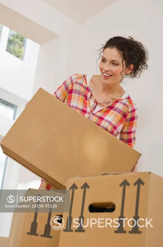 Germany, Bavaria, Grobenzell, Mid adult woman carrying cardboard boxes in house, smiling