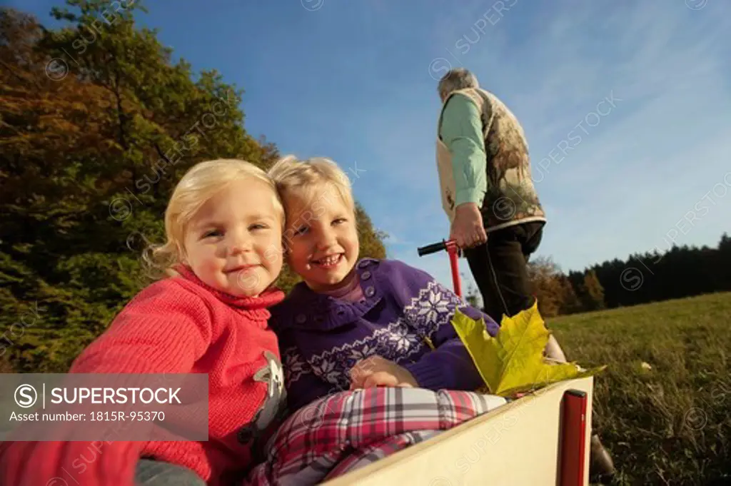 Germany, Bavaria, Grandfather pulling granddaughters sitting in wagon