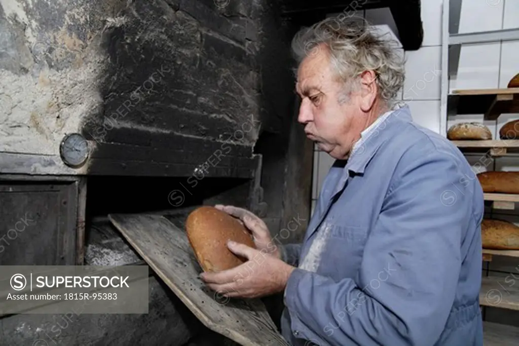 Germany, Upper Bavaria, Egling, Senior man baking bread in wood stove bakery