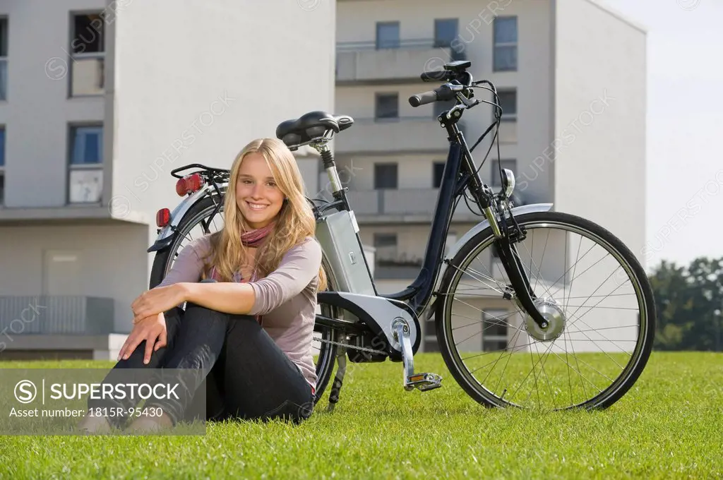Germany, Bavaria, Teenage girl sitting in grass by bicycle, smiling, portrait