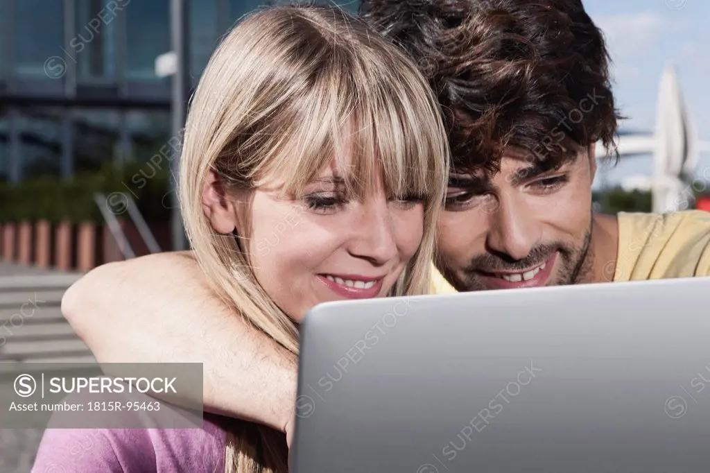 Germany, Cologne, Young couple using laptop, smiling