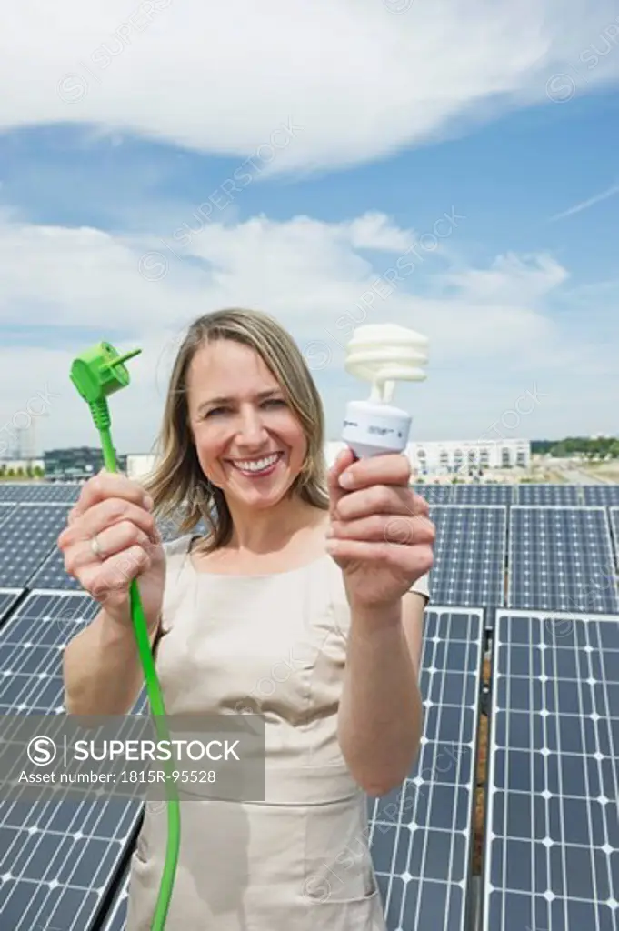 Germany, Munich, Woman holding electric cord and lightbulb in solar energy, smiling, portrait