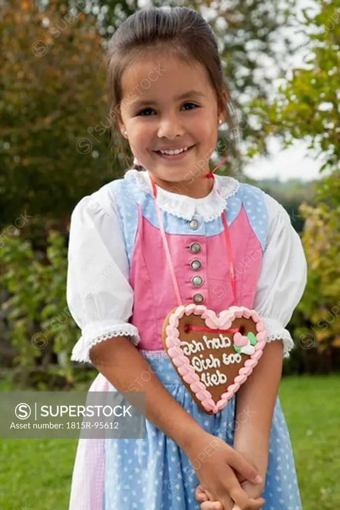 Germany, Bavaria, Huglfing, Girl with gingerbread heart in garden, smiling, portrait
