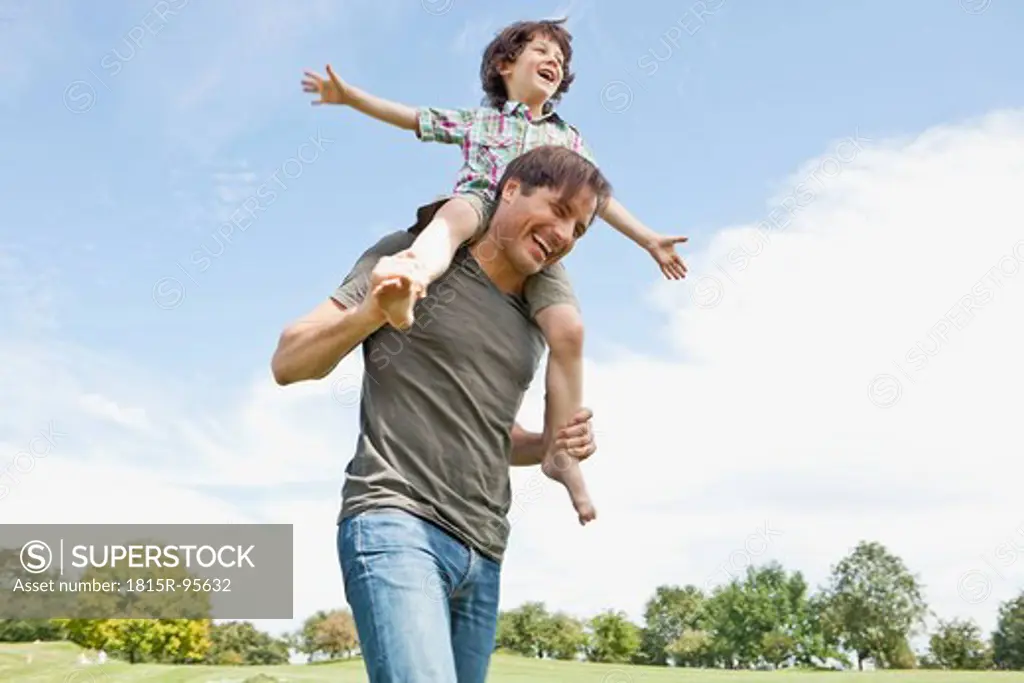 Germany, Bavaria, Father carrying son on shoulder in park, smiling