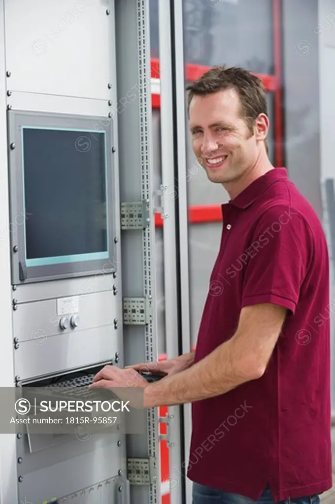 Germany, Munich, Technician standing near switch cabinet, smiling, portrait