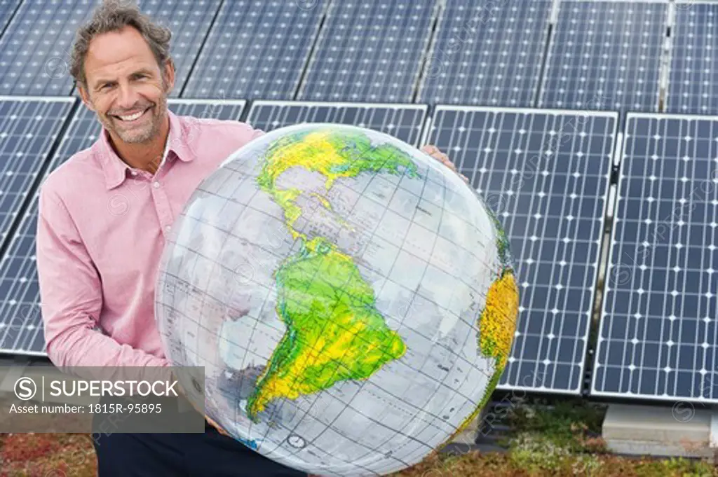 Germany, Munich, Mature man holding globe in solar plant, smiling, portrait