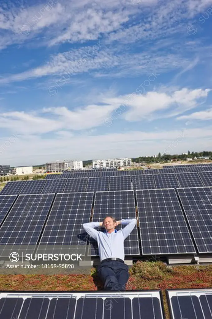 Germany, Munich, Mature man resting on panel in solar plant, smiling