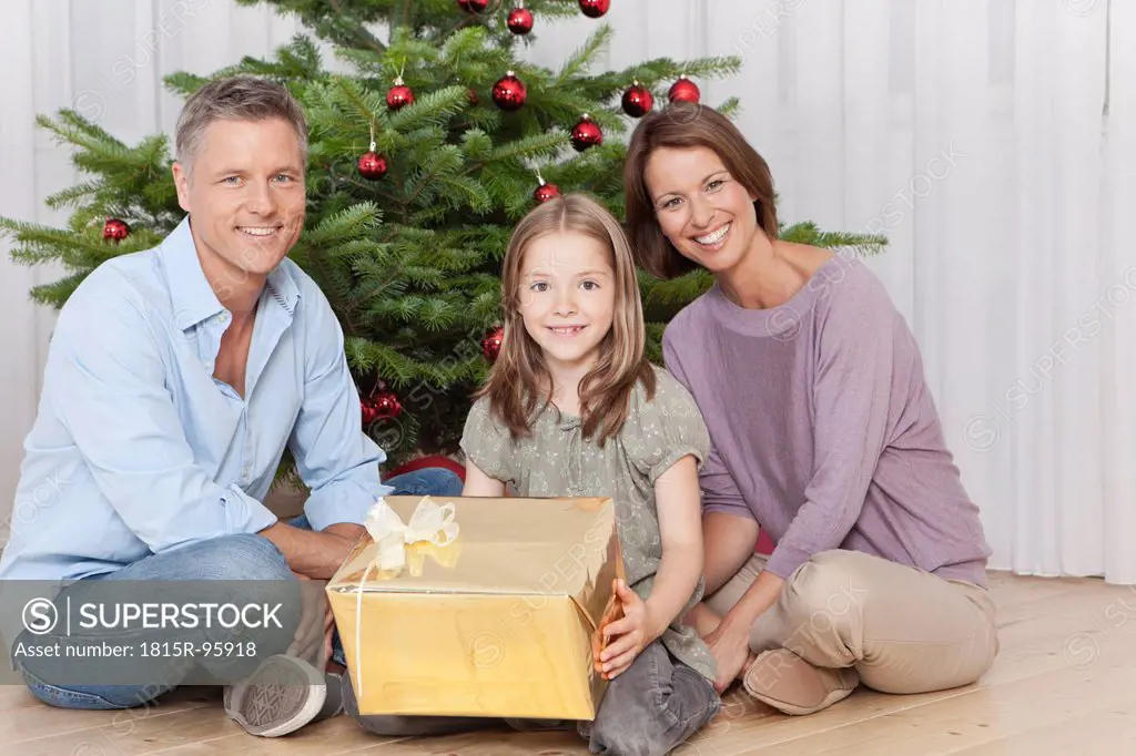 Germany, Munich, Family sitting by christmas tree with gift, smiling, portrait