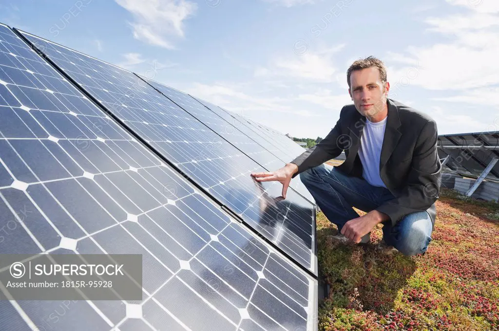 Germany, Munich, Man touching solar panel in solar plant, smiling, portrait