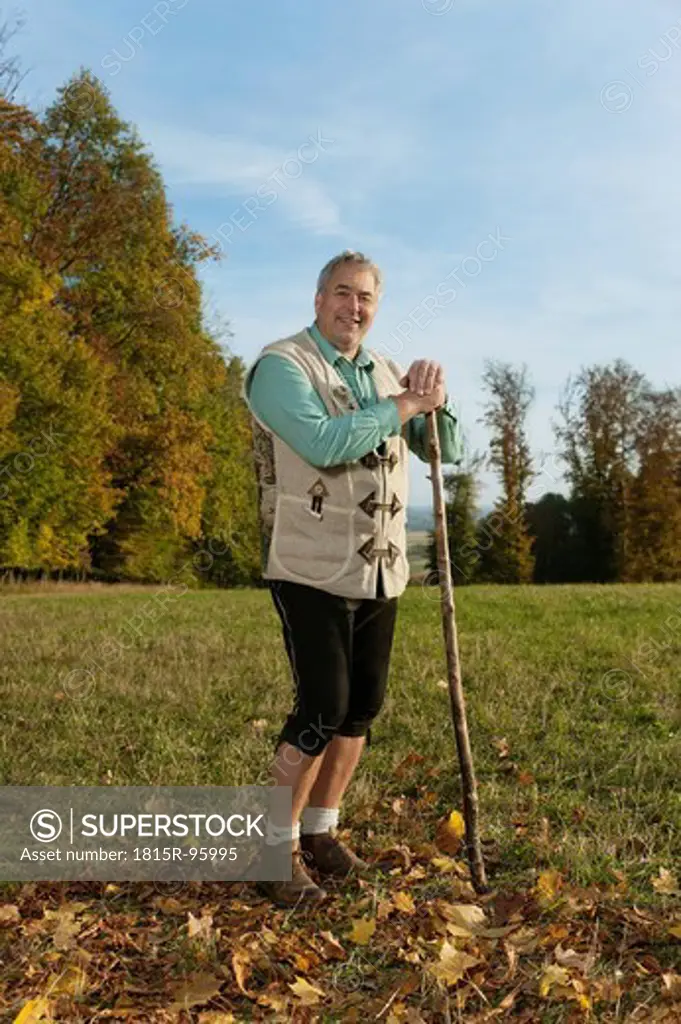 Germany, Bavaria, Mature man in traditional vest with cane, smiling, portrait